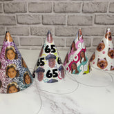 Five party hats with personalized designs on a white surface with a brick wall background.